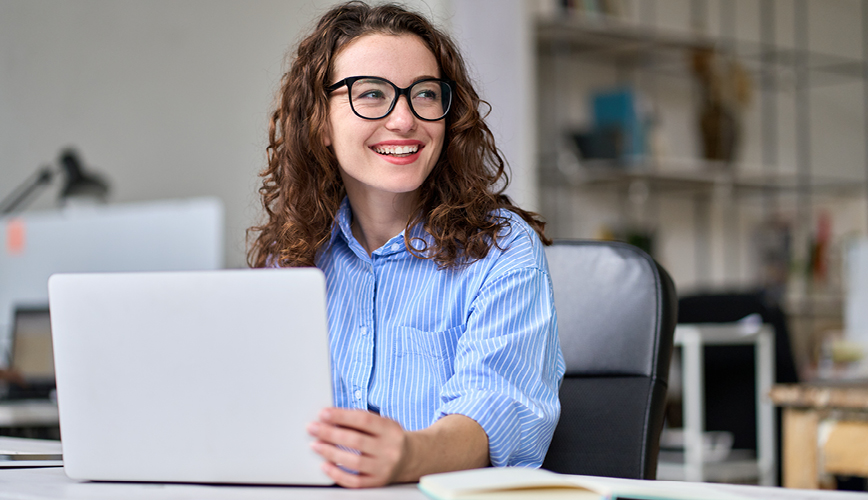 Woman sitting at a desk in front of her laptop smiling.